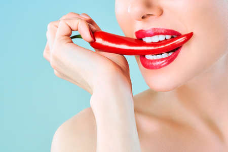 Young woman with chili red pepper isolated en blue background. Sexy female lips. Hot seductive girl