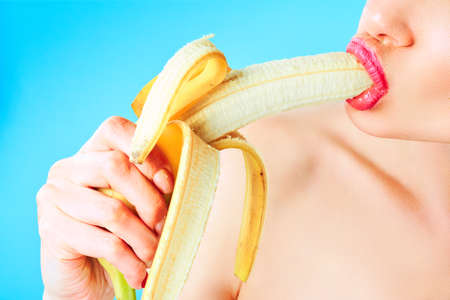 Close-up of sexy woman eating banana isolated on blue.の写真素材