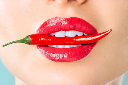 Young woman with chili red pepper isolated en blue background. Sexy female lips. Hot seductive girl