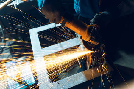 Locksmith in special clothes and goggles works in production. Metal processing with angle grinder....