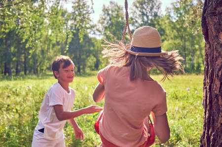 Children play and laugh in nature. A boy shakes a girl in a swing. Lifestyle photoの写真素材