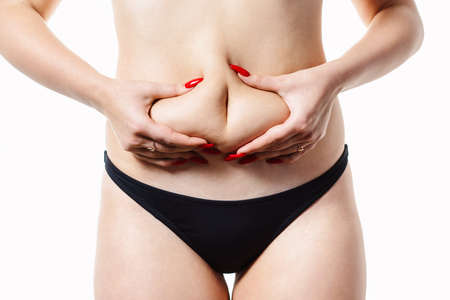 Woman holds a fold of fat on her waist. Conceptual image of obesity. Close-up, Isolated on a white background.の写真素材