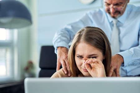 Harassment with a boss touching the arm to his secretary who is sitting in his workplace at officeの写真素材