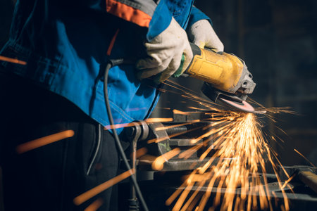 Locksmith in special clothes and goggles works in production. Metal processing with angle grinder....