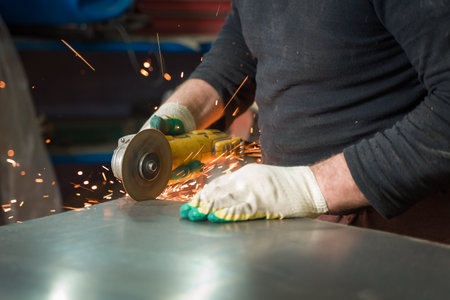 Locksmith in special clothes and goggles works in production. Metal processing with angle grinder....