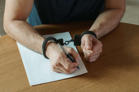 Men hands with handcuffs fill the police record, confession. on top of the police investigative detective. Arrest, bail, criminal, prison. fingerprints, criminal.の写真素材