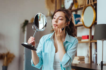 Young pretty woman does makeup at home while looking in the mirrorの写真素材
