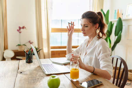 A young woman works at a laptop in a home office.