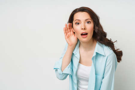 A young woman eavesdrops on someone elses conversation with her hand to her ear. The concept of...