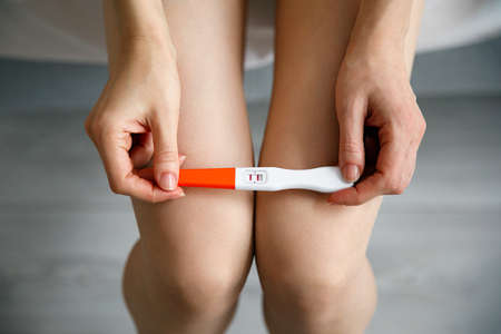 A sad young woman holds a pregnancy test in her hand. The concept of unwanted pregnancy.の写真素材