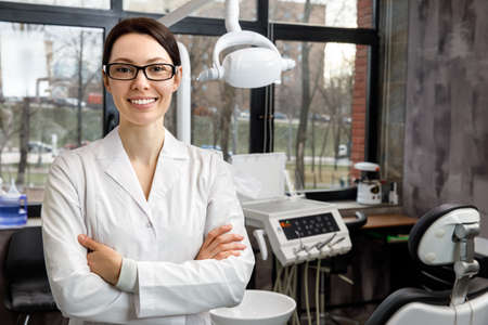 Portrait of a young female dentist on the background of the clinic. The dentist is standing with his arms crossed, looking at the camera and smiling.の写真素材