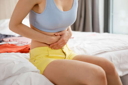 Cystitis in a woman. A young woman has a pain in the lower abdomen, she holds her stomach with her hand.の写真素材