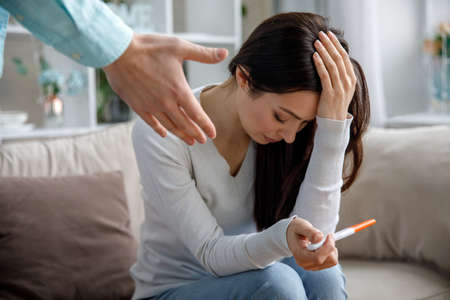 A sad young woman holds a pregnancy test in her hand. The concept of unwanted pregnancy.の写真素材