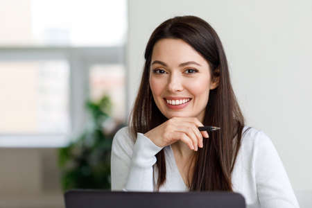 Portrait of a brunette woman working with a laptop in the office. The woman looks at the camera and smiles.の写真素材