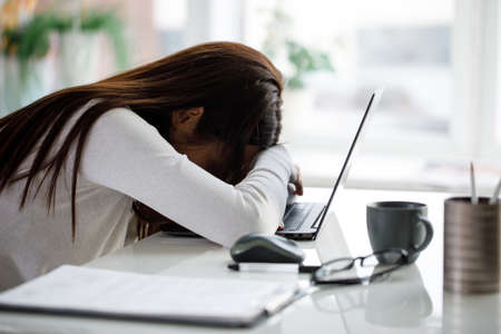 A young business woman is sitting at a table with a laptop and sleeping. The concept of overtime and...
