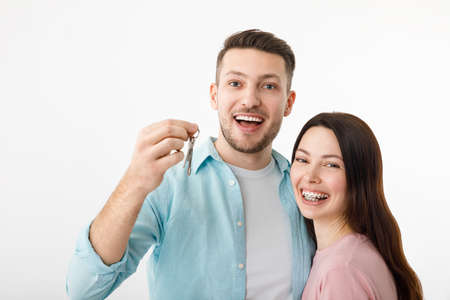 A cheerful young couple is hugging in the kitchen, holding the keys to a new house in their hands. Happy newlyweds moved into a new apartment, got a mortgage, moving day.の写真素材