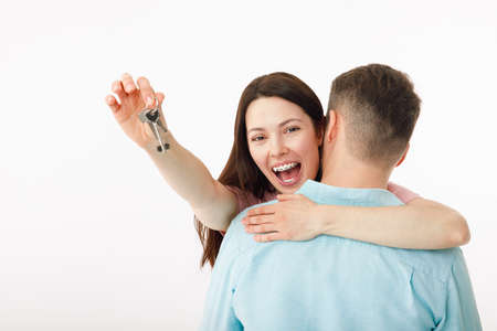 A cheerful young couple is hugging in the kitchen, holding the keys to a new house in their hands. Happy newlyweds moved into a new apartment, got a mortgage, moving day.の写真素材
