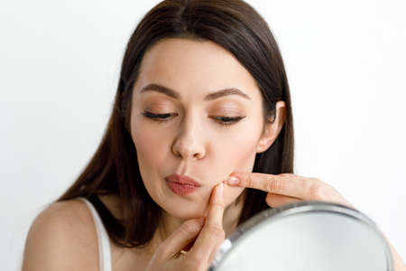A woman crushes a pimple while looking in the mirror.の写真素材