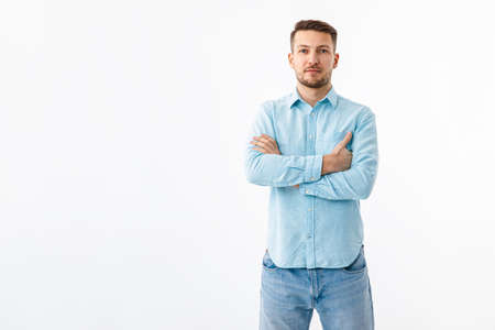 Portrait of a cheerful young man in a blue shirt on a white background. The guy stands, looks at the camera and smiles.の写真素材