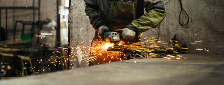 Locksmith in special clothes and goggles works in production. Metal processing with angle grinder....