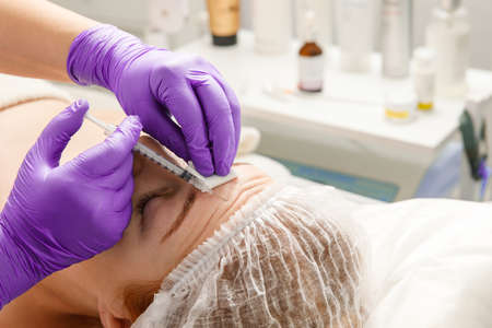 A cosmetologist performs a procedure of rejuvenating injections for the face to tighten and smooth...