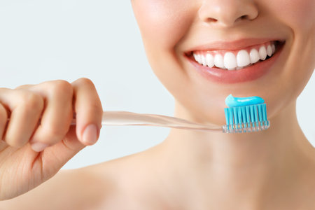 Close-up female smile. Woman holding a toothbrush and smiling with bright white teeth on isolated background, Dental oral health concept.の写真素材