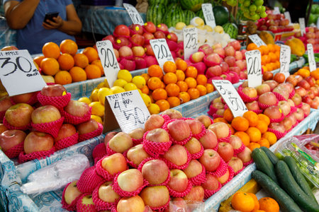Apples, oranges, lemons, and cucumbers displayed at fruit and vegetable market stall in Philippines with price signsの写真素材