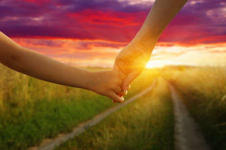 Hands of holding each other in field on road and sunの写真素材