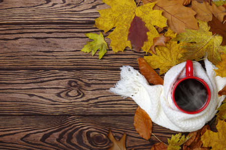 Hot cup of coffee and a scarf on wooden table background. Autumn leaves. Seasonal, still life...