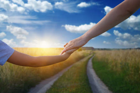 Hands of holding each other in field on road and sun