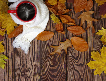 Hot cup of coffee and a scarf on wooden table background. Autumn leaves. Seasonal, still life concept.の写真素材