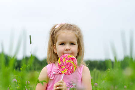 cute little girl eating a lollipop on the field の写真素材