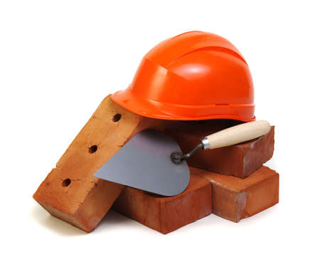 Brick, red hard hat and tools isolated on white background