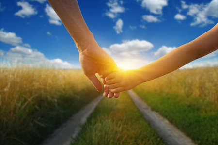 Hands of holding each other in field on road and sunの写真素材