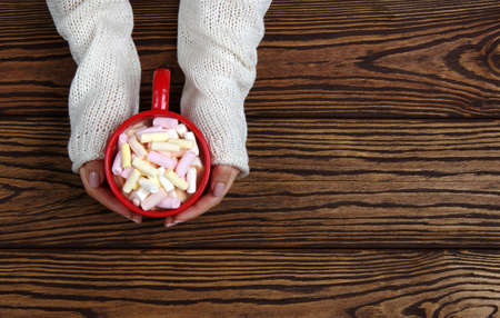 female hand holding cup of hot chocolate with marshmallow on wooden tableの写真素材