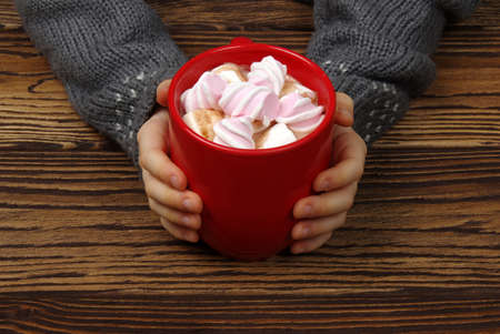 female hand holding cup of hot chocolate with marshmallow on wooden table