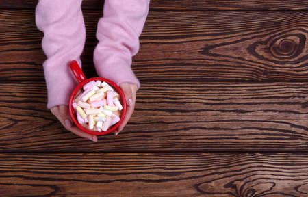 female hand holding cup of hot chocolate with marshmallow on wooden tableの写真素材