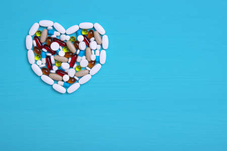 Pharmaceutical medicine pills, tablets and capsules in the shape of a heart on a blue background