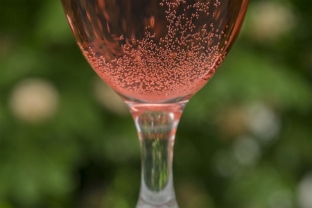 Glass of red wine with bubbles and a green backgroundの写真素材