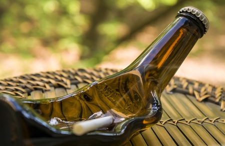 Glass beer bottle ashtray on a cane pan by the open windowの写真素材