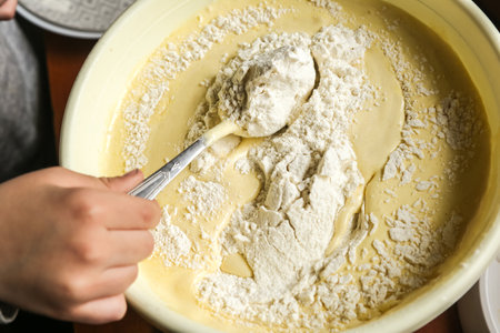 the process of making dough with the hands of a child in a yellow toe with a spoon on a dark wooden...