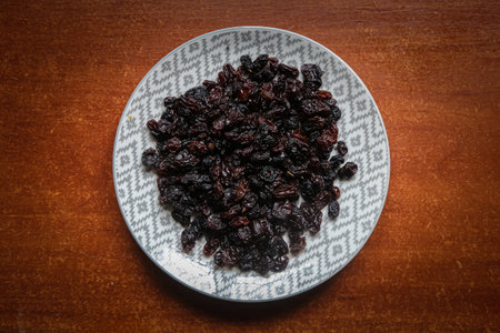 raisins dried grapes on a plate on a dark wooden table, an ingredient for baking and dessertsの写真素材