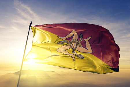 Sicily region of Italy flag textile cloth fabric waving on the top sunrise mist fogの写真素材