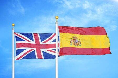 United Kingdom and Spain two flags on flagpoles and blue cloudy sky backgroundの写真素材