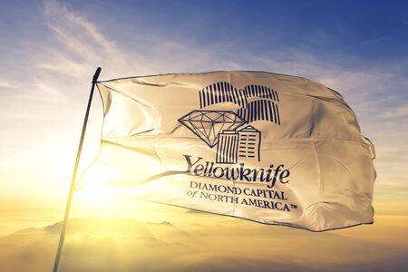 Yellowknife of Northwest Territories of Canada flag textile cloth fabric waving on the top sunrise mist fogの写真素材