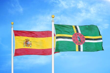 Spain and Dominica two flags on flagpoles and blue cloudy sky backgroundの写真素材
