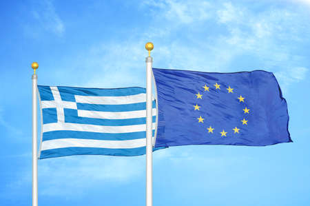 Greece and European Union two flags on flagpoles and blue cloudy sky backgroundの写真素材