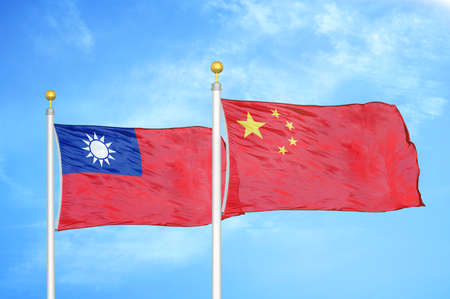 Taiwan and China two flags on flagpoles and blue cloudy sky backgroundの写真素材