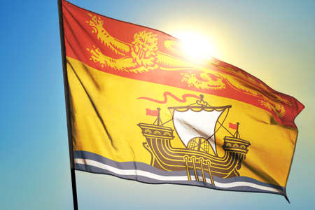 New Brunswick province of Canada flag waving on the wind in front of sunの写真素材
