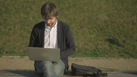 Young Man Sitting On Park Bench, Working On His Laptop, Outdoor, 4K, UHDの写真素材
